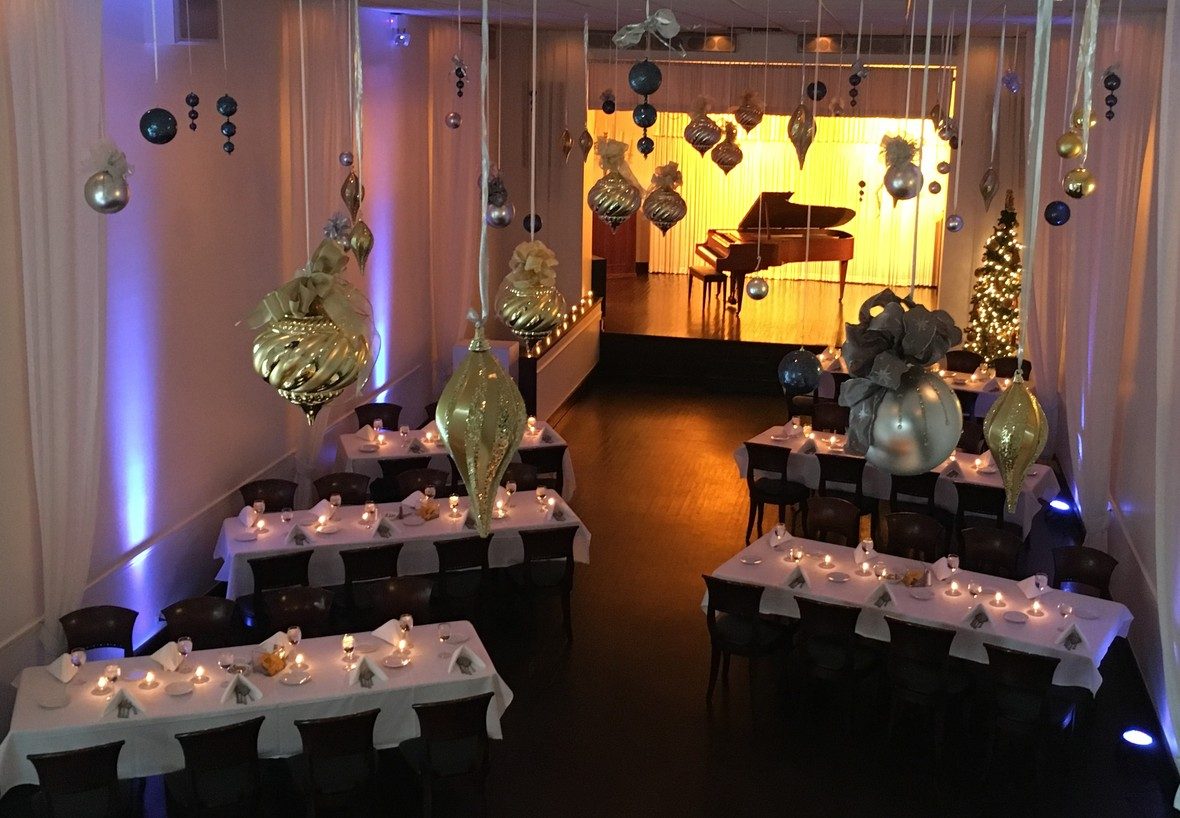 The Old Eagle Room dressed for a holiday event, with hanging ornaments and a candlelit grand piano stage